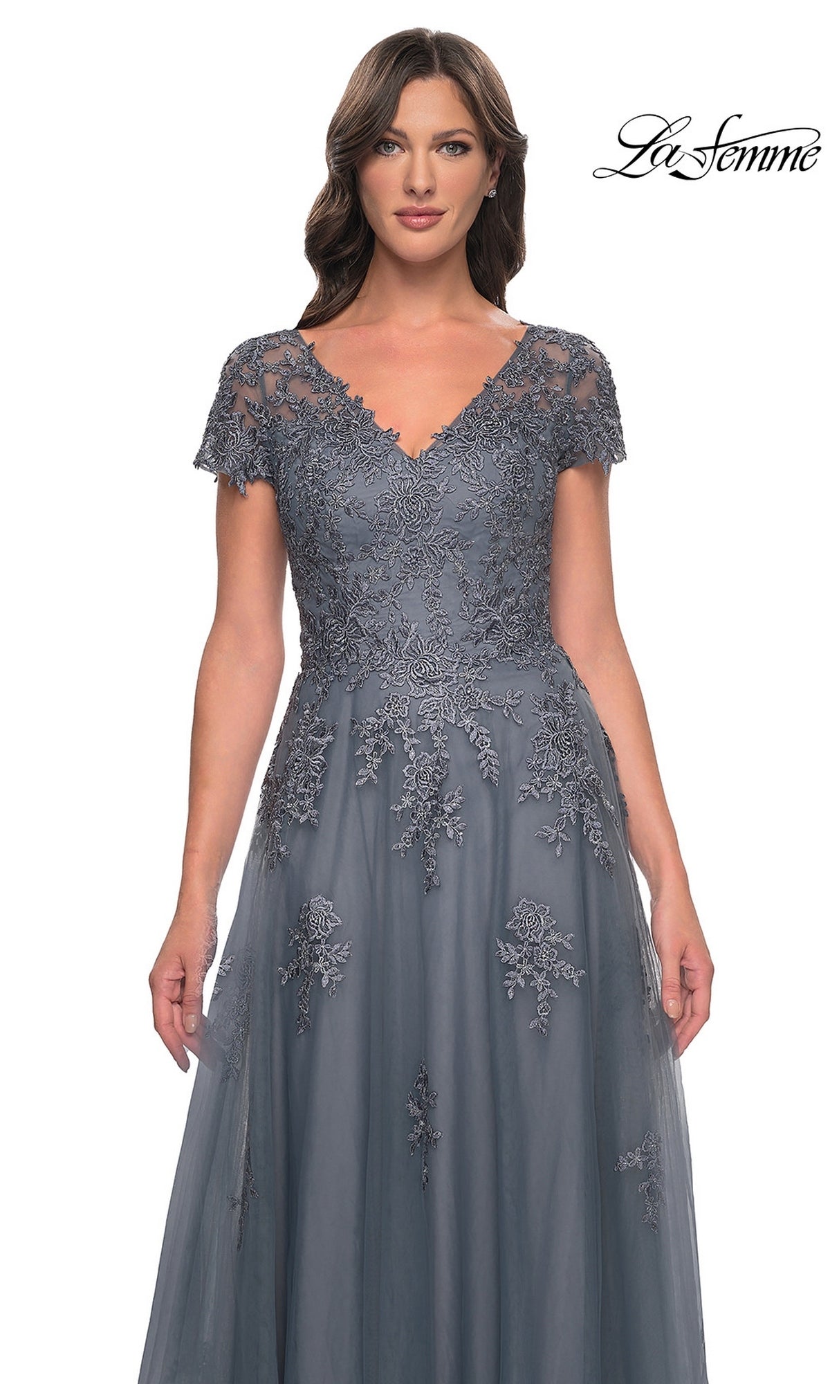 A woman wears the Long Formal Dress: La Femme 30228, a grey, floor-length V-neck tulle evening gown featuring short sleeves and detailed floral embroidery on the bodice.